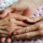 A geriatrician holds the hand of an elderly woman with arthritis.